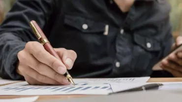 Persona escribiendo en gráficos con un bolígrafo y sosteniendo un teléfono.