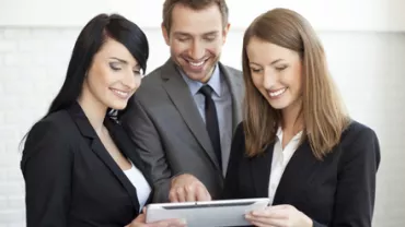 Personas en traje mirando una tableta con sonrisas.