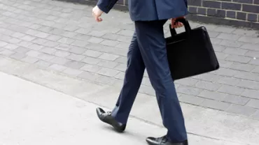 Persona caminando con traje azul y maletín negro.