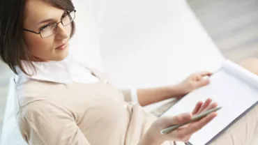 Persona con gafas sosteniendo un cuaderno y un bolígrafo.