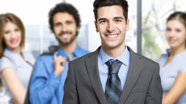 Persona sonriendo en traje, con grupo profesional atrás.