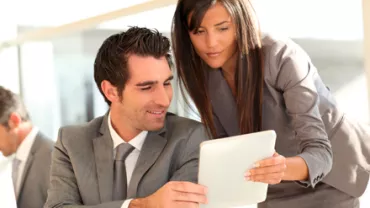 Dos personas en trajes formales revisando una tableta en una oficina.